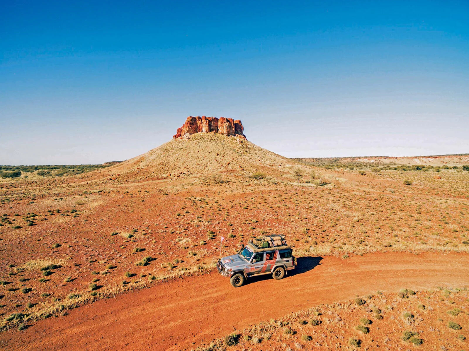 Hema Map Patrol 4WD on a red dirt track below a rocky mesa in the Australian desert