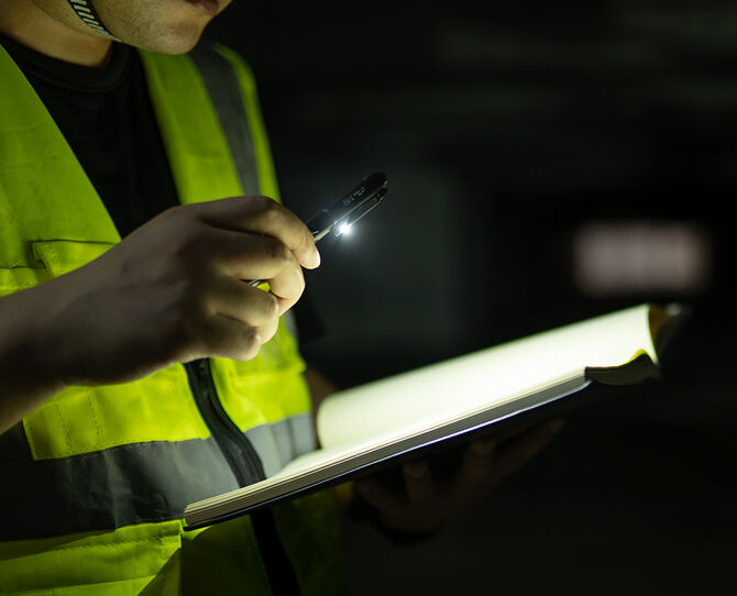 Olight Open Pro in black lighting a notebook while writing