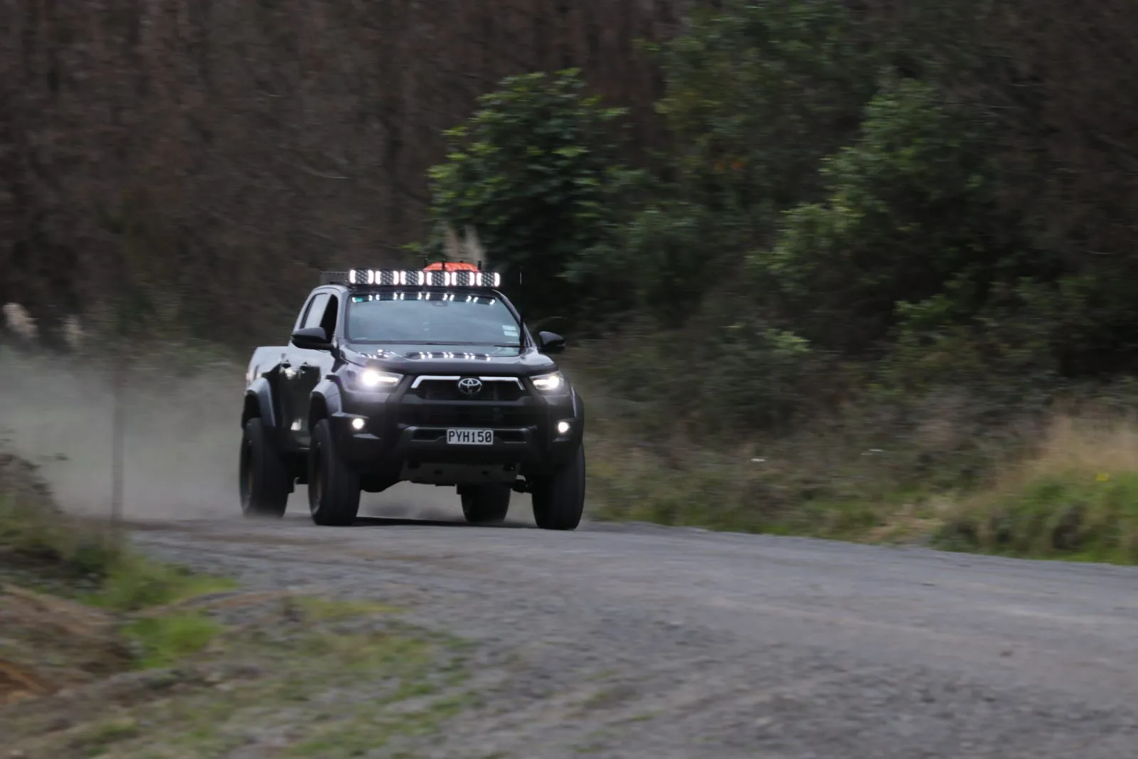Toyota Hilux with Apex Quad driving lights on at dusk on a gravel road